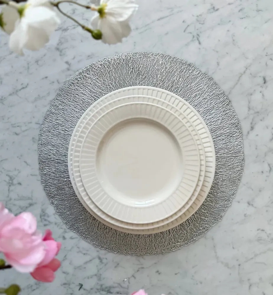 Mesa puesta con plato blanco sobre individual plateado y flores